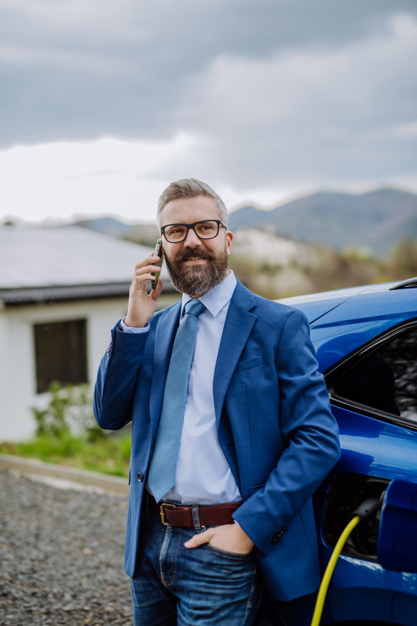 Mature businessman waiting for charging his new electric car.