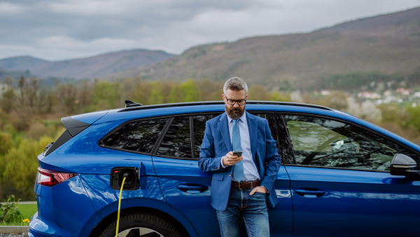 Mature businessman waiting for charging his new electric car.