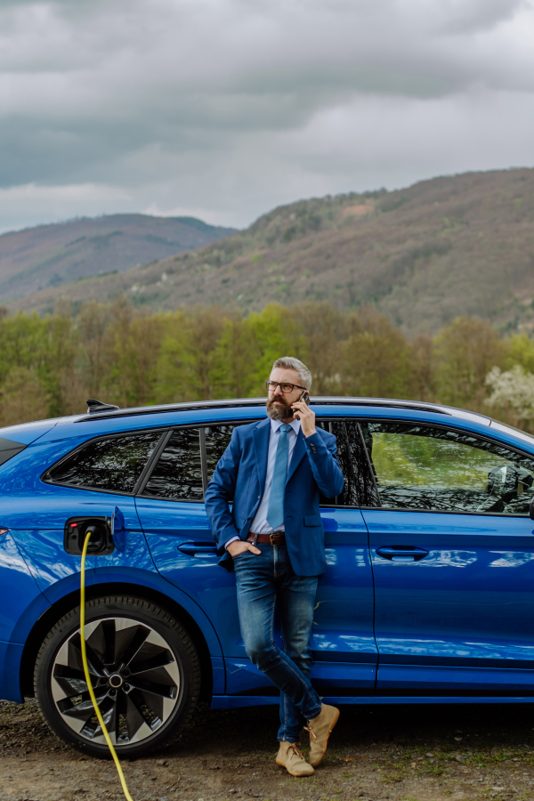 Mature businessman waiting for charging his new electric car.