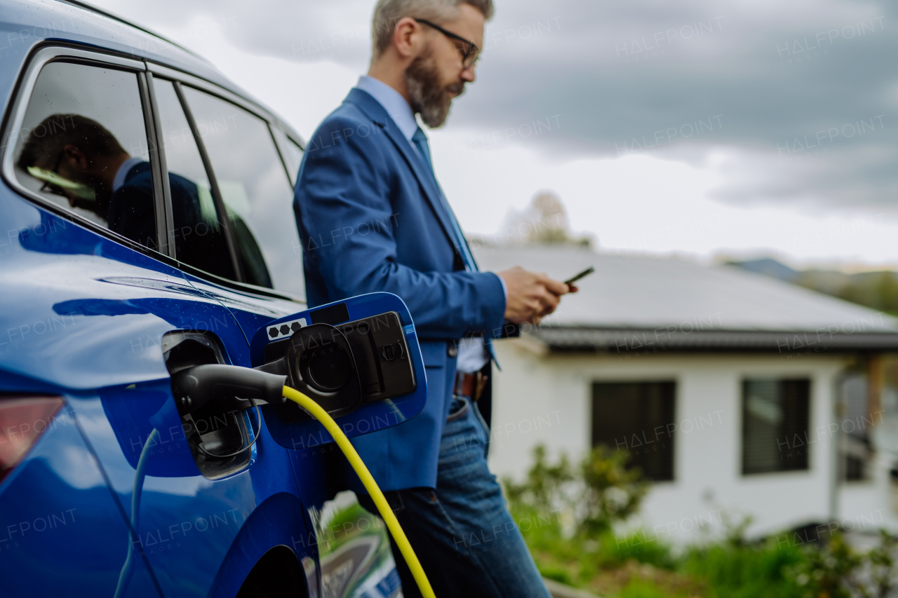 Mature businessman waiting for charging his new electric car.