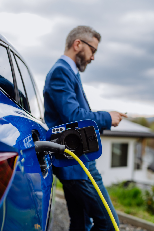 Mature businessman waiting for charging his new electric car.