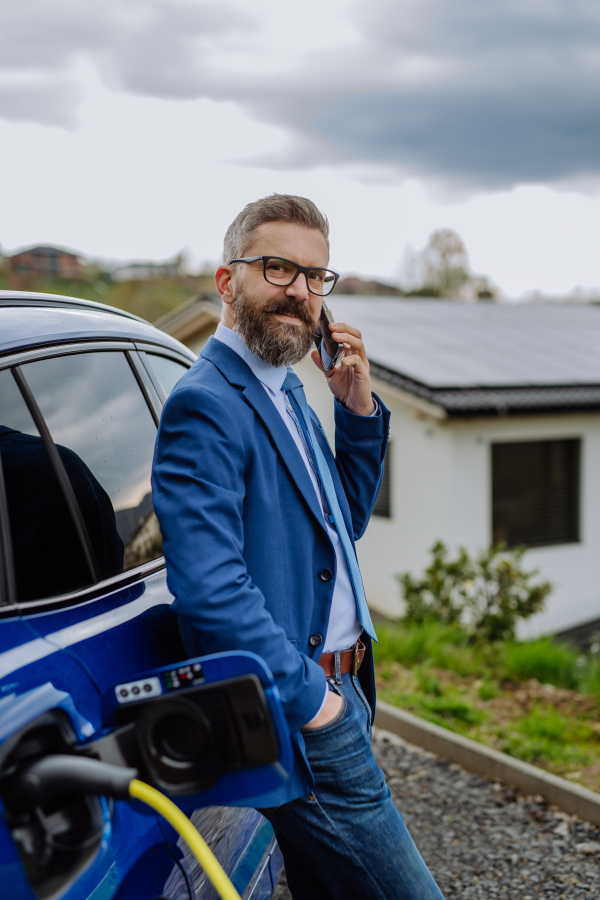 Mature businessman waiting for charging his new electric car.