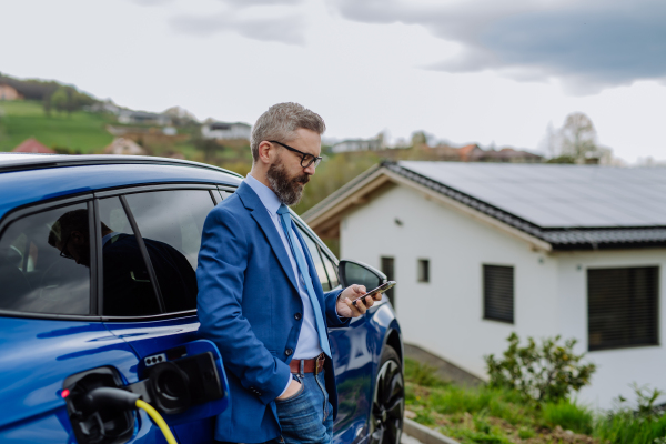 Mature businessman waiting for charging his new electric car.