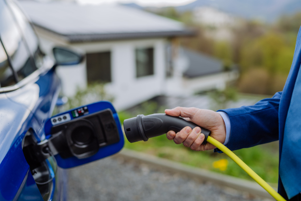 Mature businessman holding power supply cable and charging his new electric car.