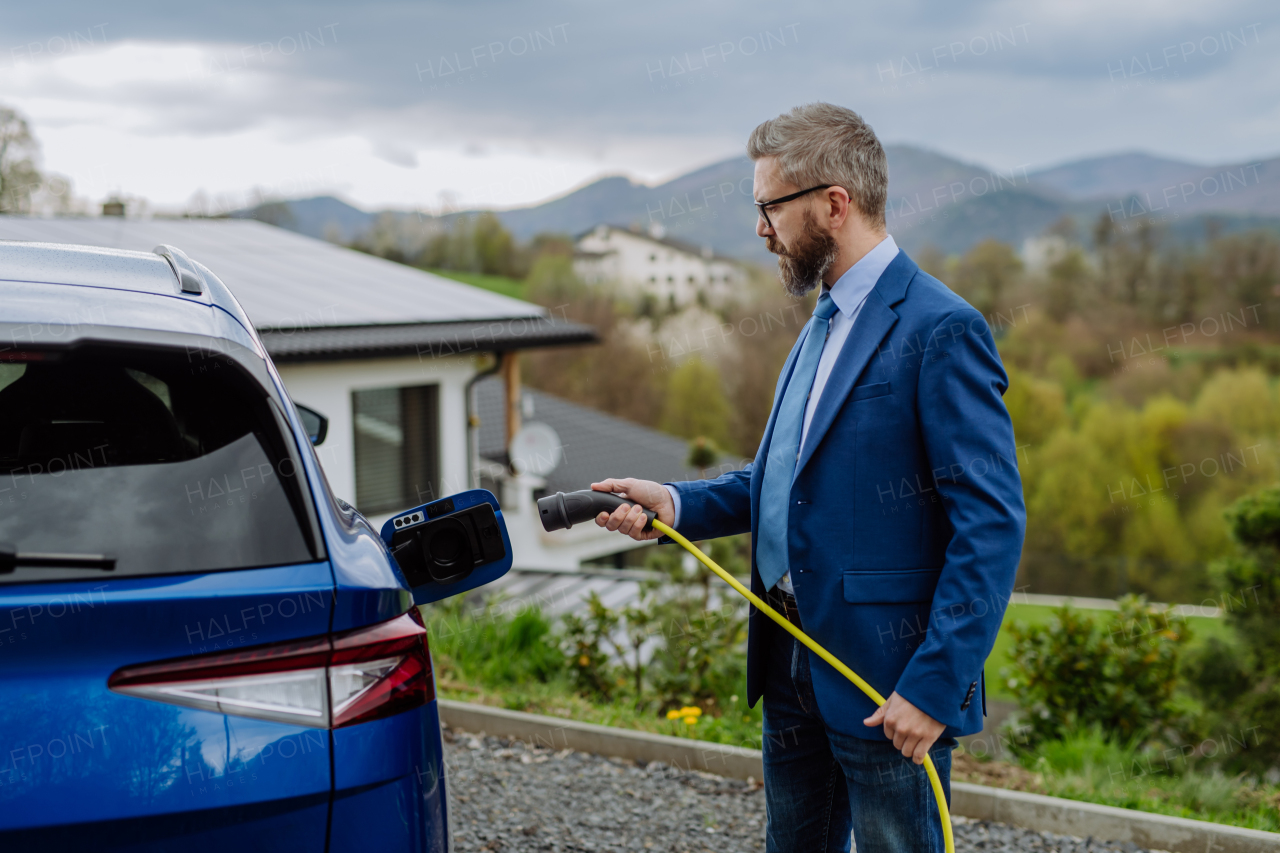 Mature businessman holding power supply cable and charging his new electric car.