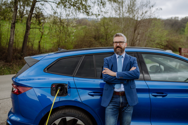 Mature businessman waiting for charging his new electric car.