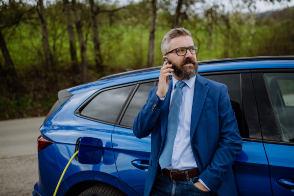 Mature businessman waiting for charging his new electric car.