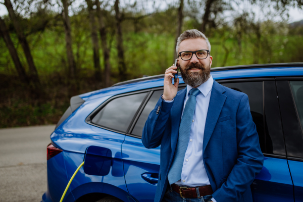 Mature businessman waiting for charging his new electric car.