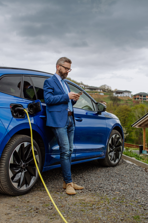 Mature businessman waiting for charging his new electric car.