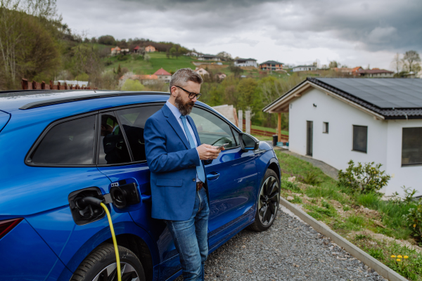 Mature businessman waiting for charging his new electric car.