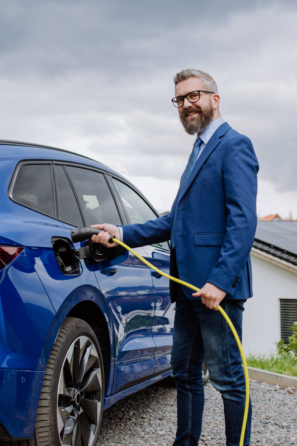 Mature businessman holding power supply cable and charging his new electric car.