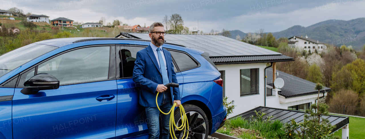 Mature businessman holding power supply cable from his new electric car.