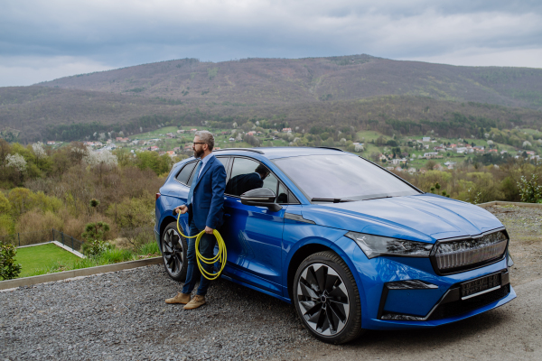 Mature businessman holding power supply cable from his new electric car.