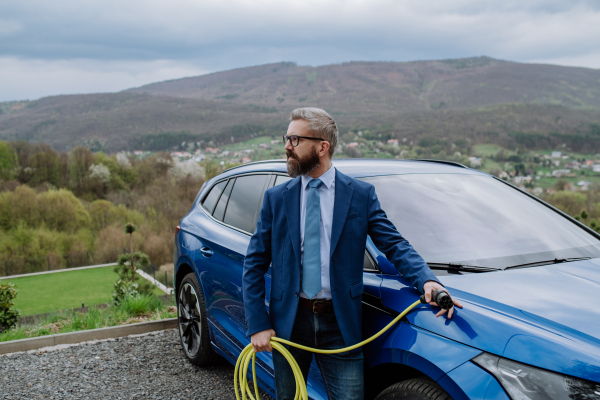 Mature businessman holding power supply cable from his new electric car.