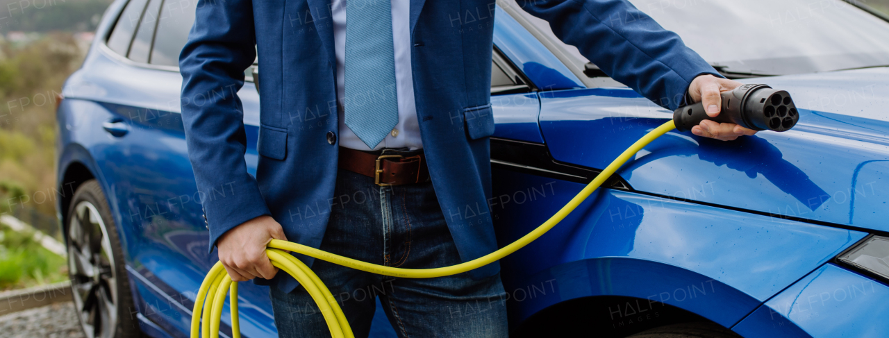 Close up of businessman holding power supply cable from his new electric car.