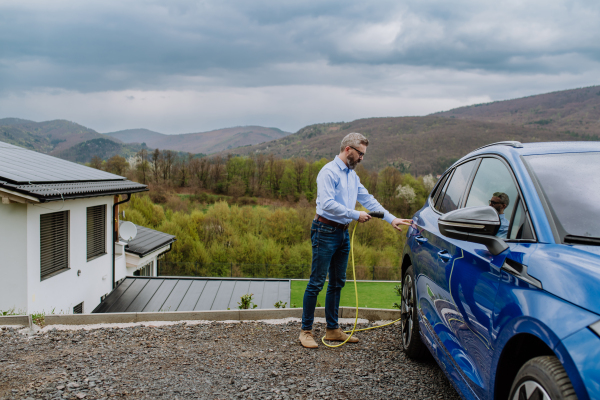 Mature businessman holding power supply cable and charging his new electric car.