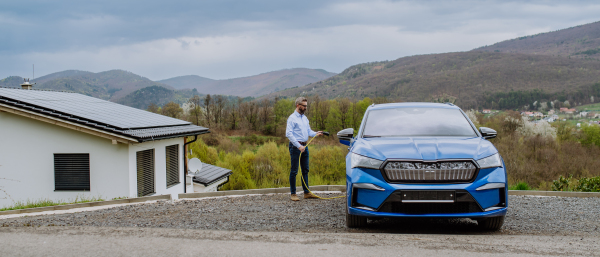 Mature businessman holding power supply cable and charging his new electric car.