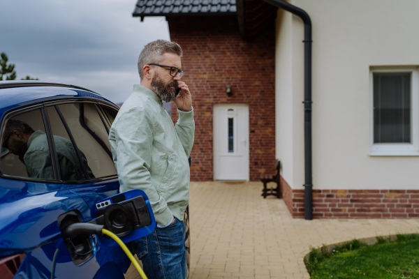 Mature businessman waiting for charging his new electric car.