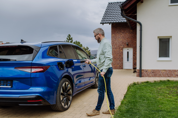 Mature man holding power supply cable and charging his new electric car.