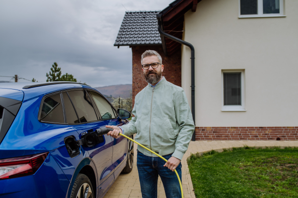 Mature businessman holding power supply cable and charging his new electric car.