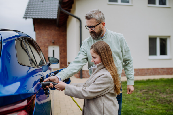 Mature man and his daughter charging their electric car.