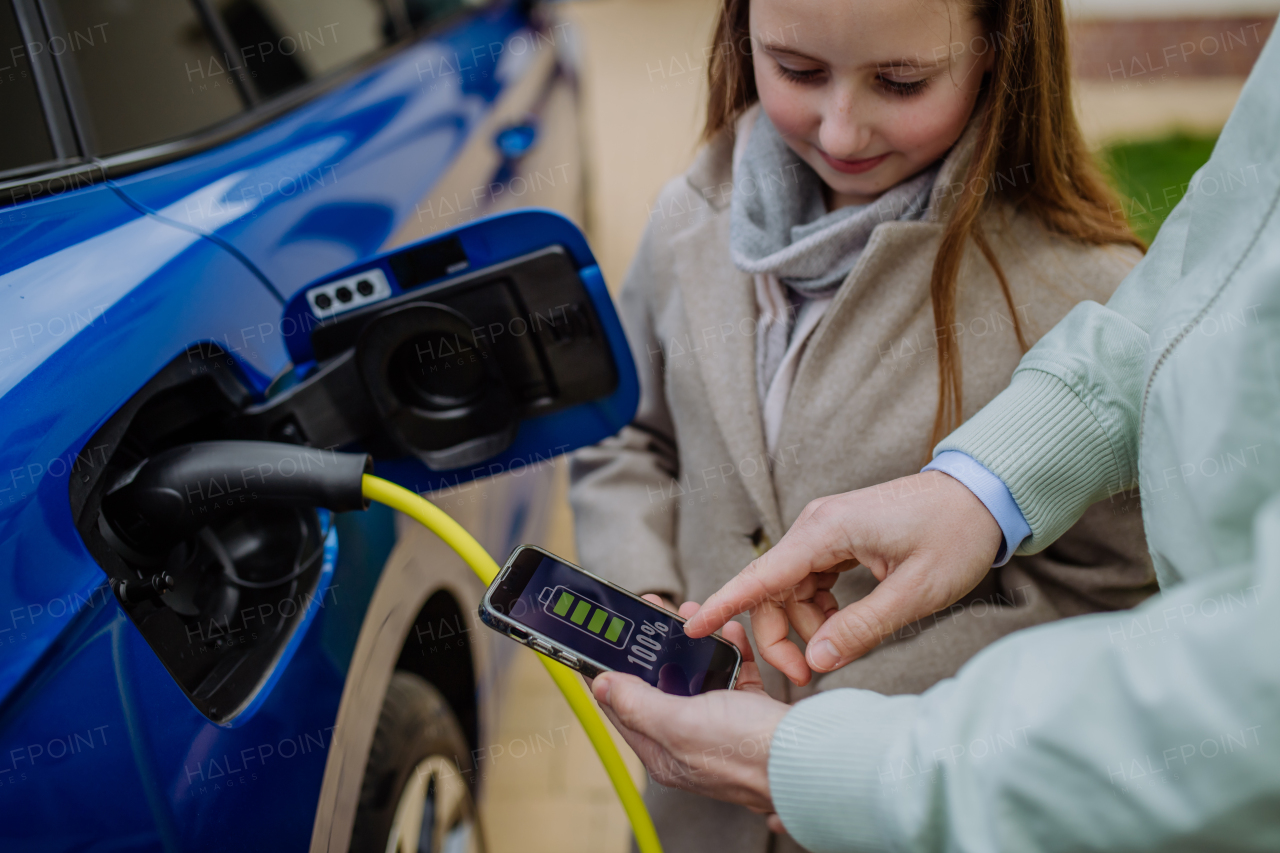 Close up of man and his daughter holding phone, checking charging of his electric car.