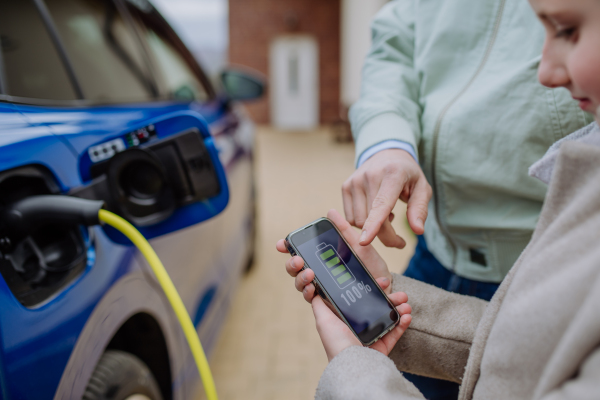 Close up of man and his daughter holding phone, checking charging of his electric car.