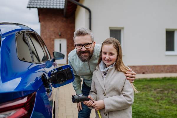 Mature man and his daughter charging their electric car.