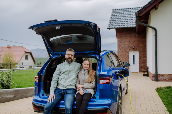 Father and his daughter waiting for charging their new electric car.