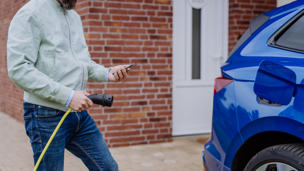 Close up of man holding power supply cable and charging his new electric car.