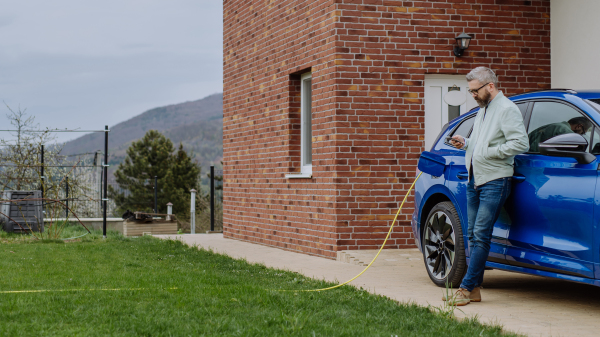 Mature businessman waiting for charging his new electric car.