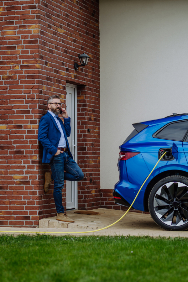 Mature businessman waiting for charging his new electric car.