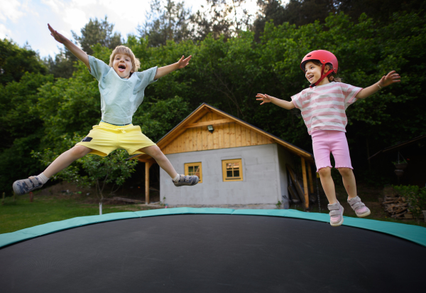 A little siblings enjoy jumping on trampoline - outside in backyard