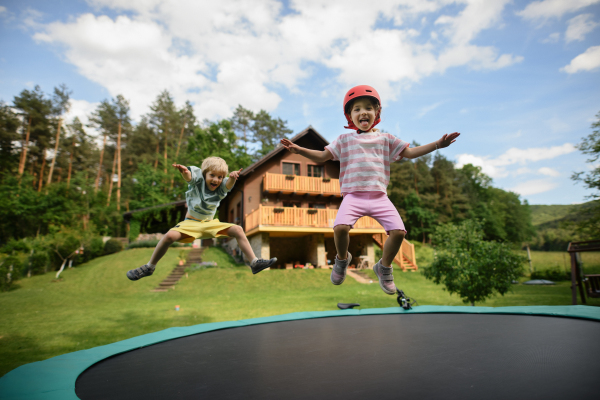 A little siblings enjoy jumping on trampoline - outside in backyard