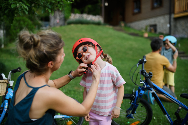 A young mother with little daughter preaparing for bike ride, putting on helmets.