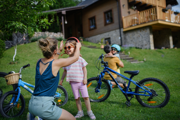 A young family with little children preaparing for bike ride, putting on helmets in front of house.