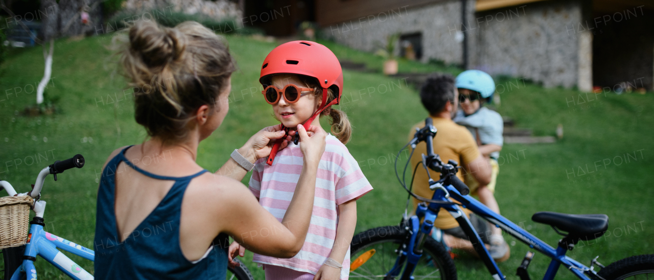 A young family with little children preaparing for bike ride, putting on helmets in front of house.