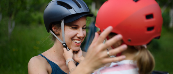 A young mother with little daughter preaparing for bike ride, putting on helmets.