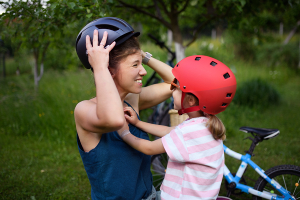 A young family with little children preaparing for bike ride, putting on helmets in front of house.