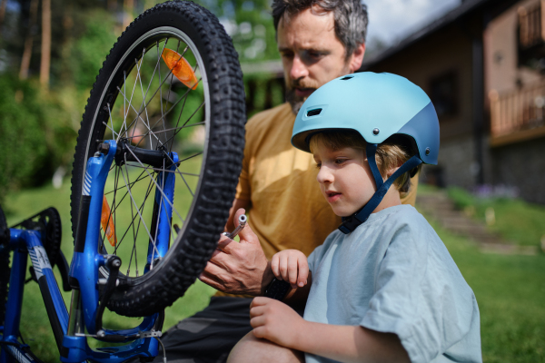 A father with little son together preparing bicycle for a ride, pumping up tyres in garden in front of house.