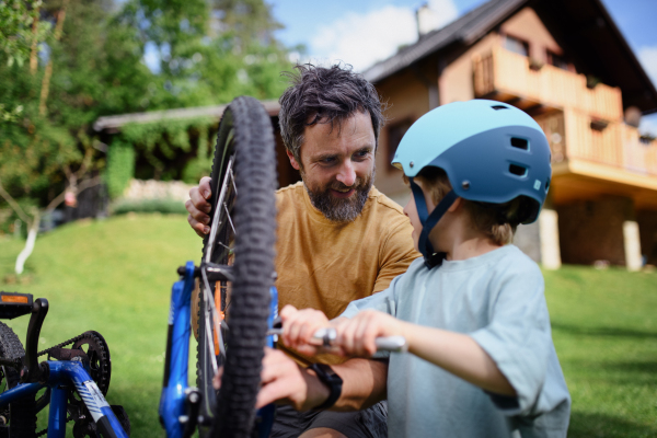 A father with little son together preparing bicycle for a ride, pumping up tyres in garden in front of house.