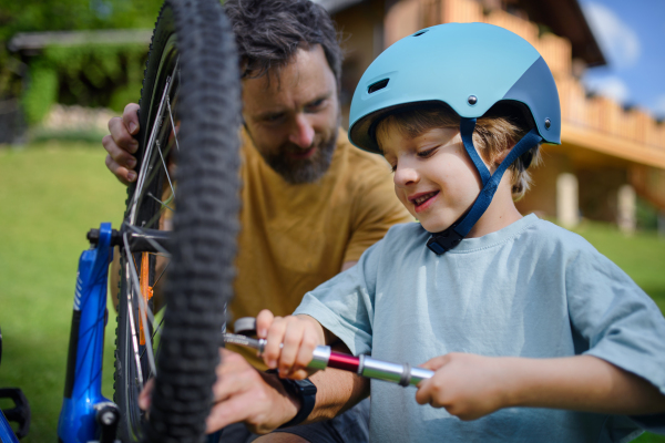 A father with little son together preparing bicycle for a ride, pumping up tyres in garden in front of house.