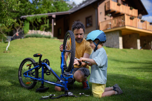 A father with little son together preparing bicycle for a ride, pumping up tyres in garden in front of house.