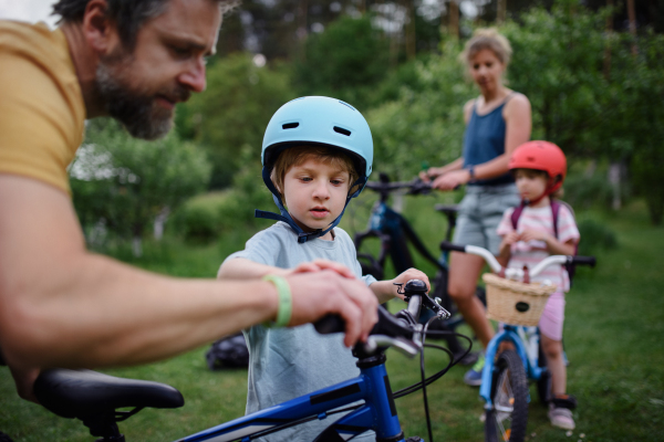 A portrait of young family with little children preapring for bike ride, standing with bicycles in nature.