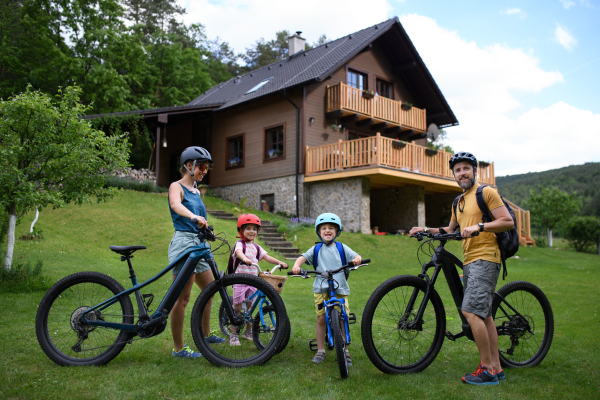 A portrait of young family with little children preapring for bike ride, standing with bicycles in front of house.