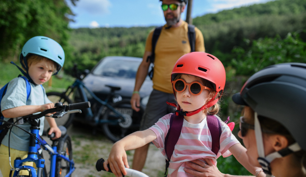 A portrait of young family with little children preapring for bike ride, standing ready with bicycles and helmet in nature.