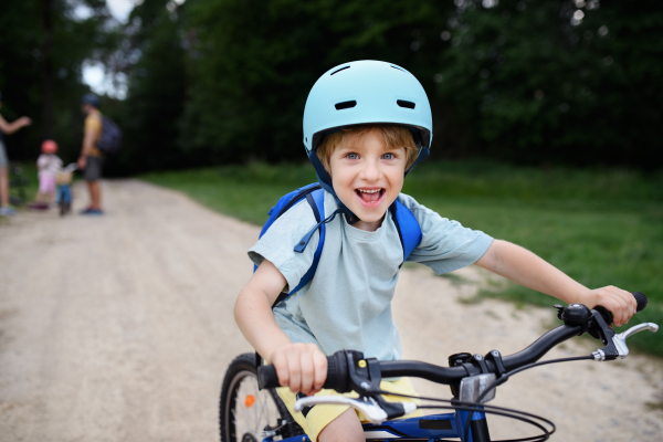 A portrait of excited little boy with his family at backround riding bike on path in park in summer