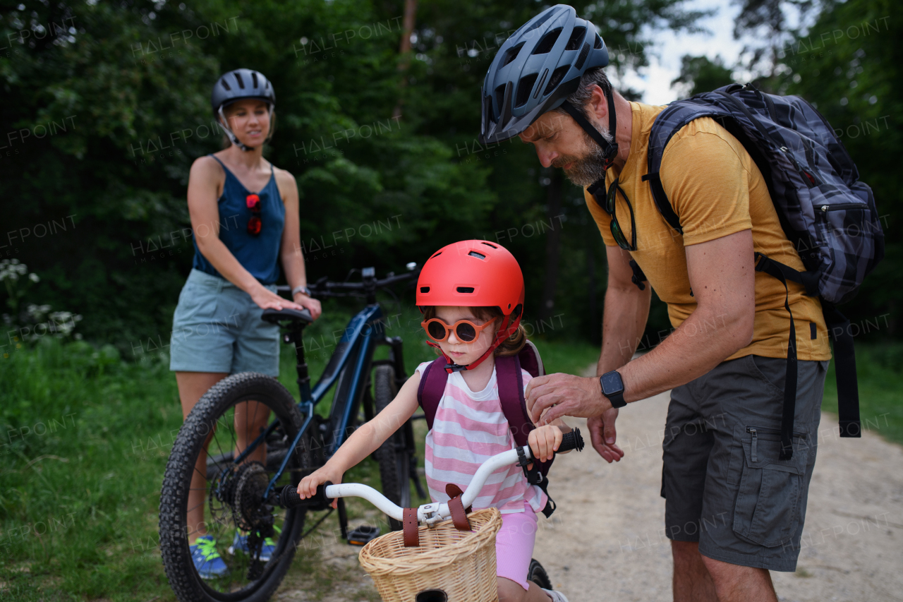 A portrait of young family with little children preapring for bike ride, standing with bicycles in nature.