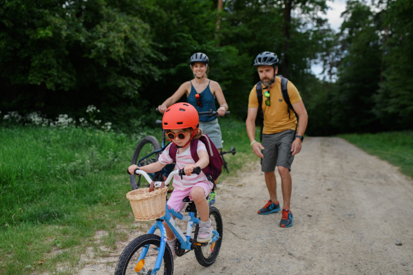 A portrait of young family with little children preapring for bike ride, standing with bicycles in nature.