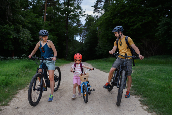 A young family with little child riding bicycles on road in village in summer.